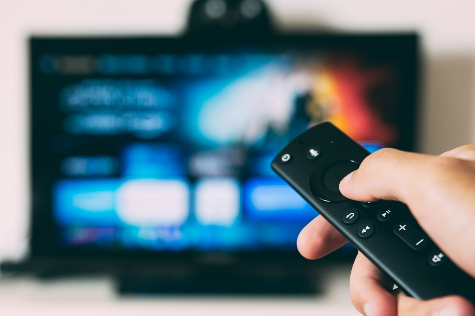 Hand pointing a remote at a TV showing a streaming app